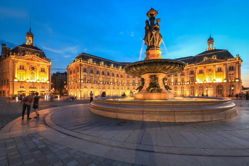 Place de la Bourse illuminée à la tombée de la nuit, fontaine des Trois Grâces
