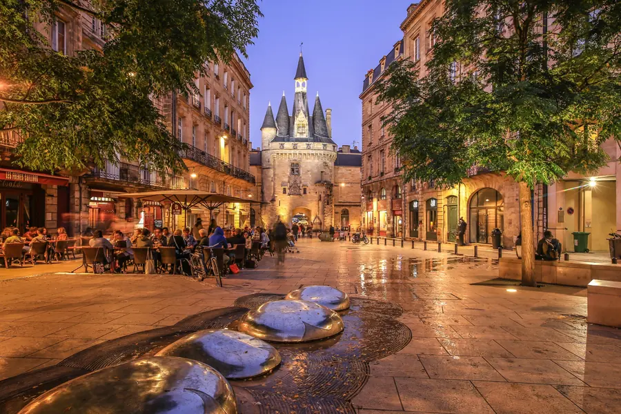Porte Cailhau éclairée le soir, terrasses de café animées